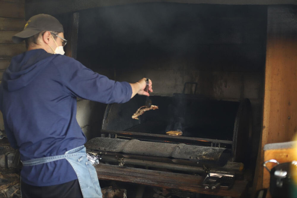 お手製の炭火焼グリルでベーコンやパティを焼くブライアンさん
