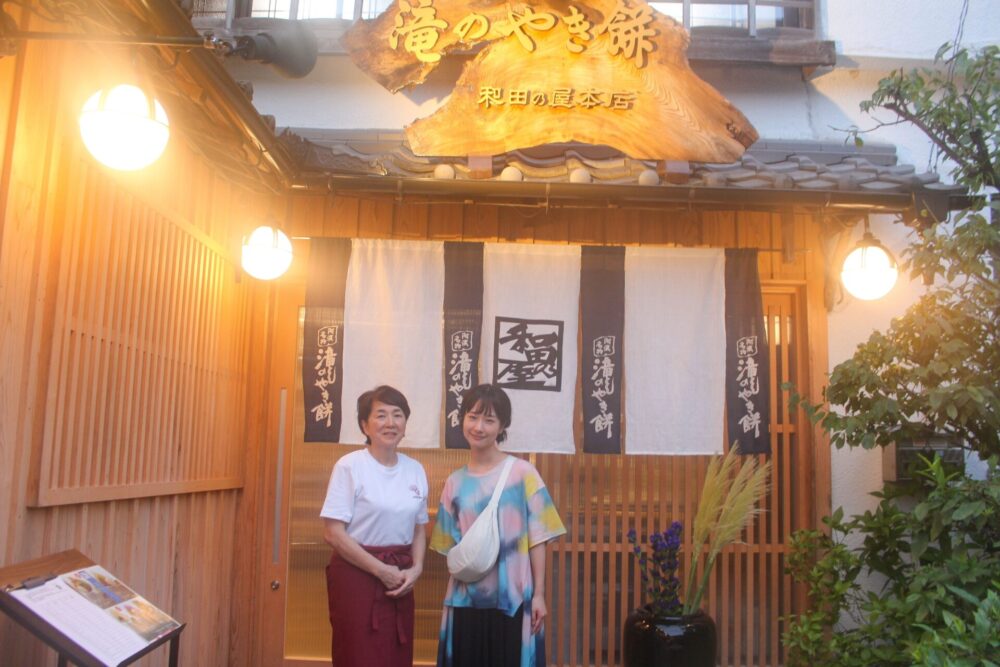 和田の屋３代目女将の和田英美さんと記念写真を撮る藤間さん