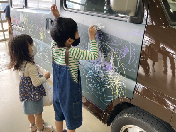 表面が黒板塗装となっている車に子どもが絵を描いている様子