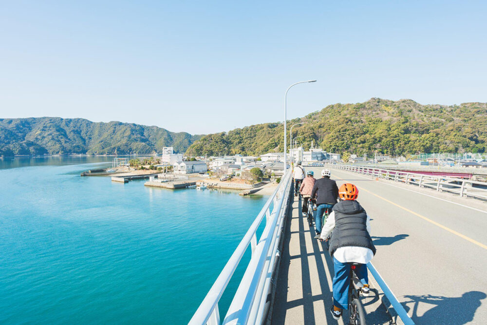 青い海と山が周辺に広がる宇佐大橋をサイクリングする人々