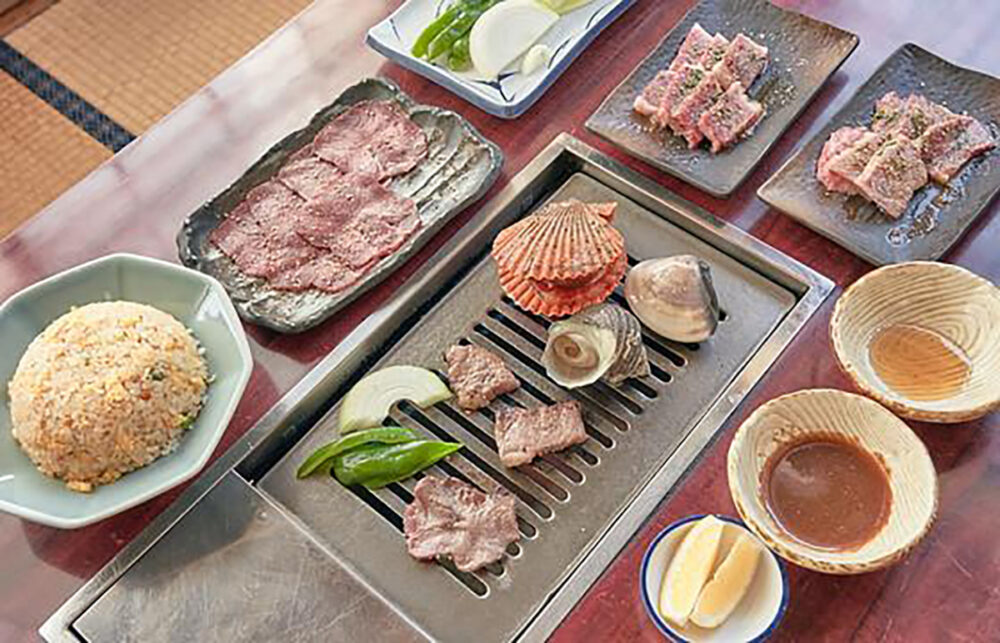 鉄板付きテーブルに並ぶ、肉や貝類、炒飯などの食事セット