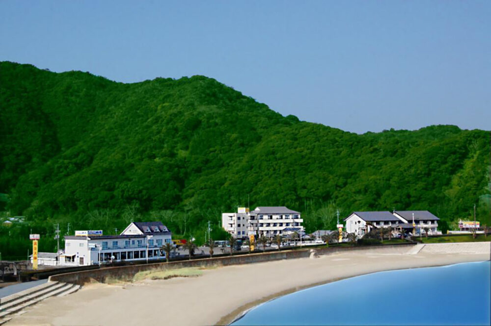 海に隣接する三陽荘の建物と背後に広がる緑の山々
