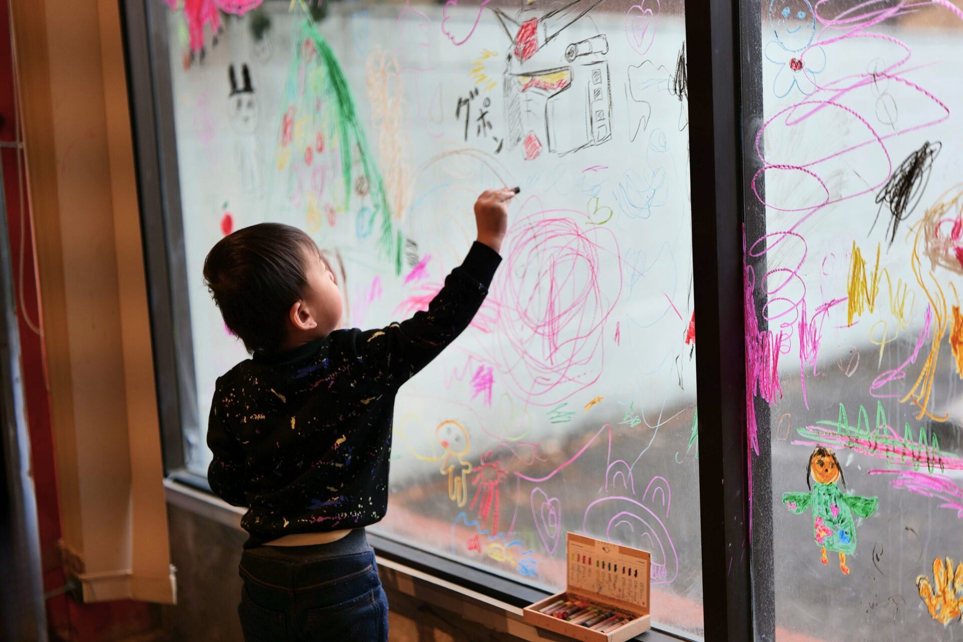 ガラス窓にカラーコンテで絵を描いて楽しむ子ども